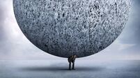 Businessman Bending Over To Support Very Large Stone Sphere On His Back