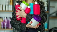 Lot of plastic bottles with cosmetics in female hands against background of shelves in store.