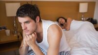 Thoughtful man sitting up with partner asleep
