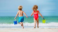 View from behind of a boy and girl run with bucket to ocean