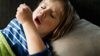 Small boy coughing from with closed eyes at home.