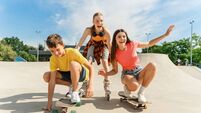 Happy friends with skateboard and roller-skates on the sports ramp playground