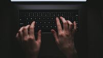 Woman is typing on a laptop keyboard while lying on a sofa at home in the dark.