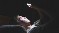 Depressed teenager on his phone in the dark.