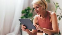 A Happy Blonde Senior Woman Watching Some Yoga Classes While Using An App On Her Tablet