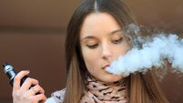 Vape teenager. Young pretty white girl in casual clothing smoking an electronic cigarette opposite modern background on the stre